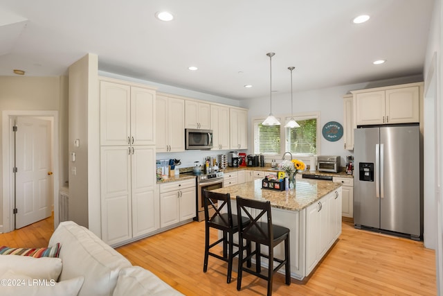 kitchen with a kitchen island, appliances with stainless steel finishes, decorative light fixtures, sink, and light hardwood / wood-style flooring