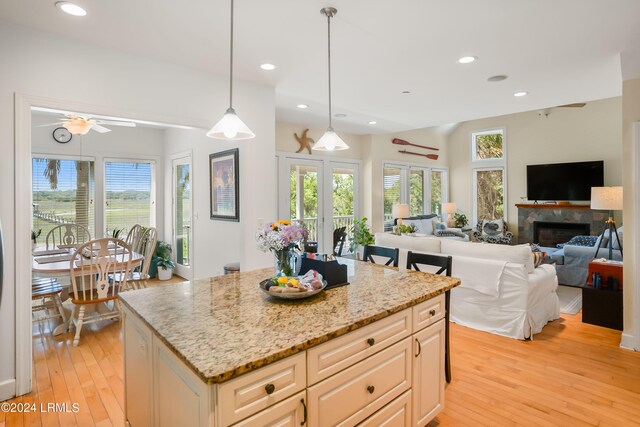 kitchen with hanging light fixtures, a kitchen island, plenty of natural light, and light stone counters