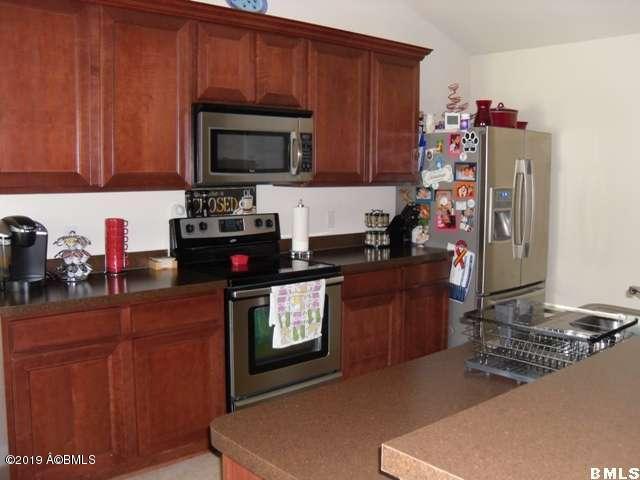 kitchen featuring brown cabinets, stainless steel appliances, dark countertops, and vaulted ceiling