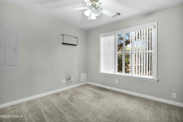 carpeted empty room with visible vents, a ceiling fan, electric panel, and baseboards