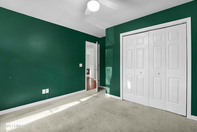 unfurnished bedroom with carpet, a closet, a ceiling fan, a textured ceiling, and baseboards