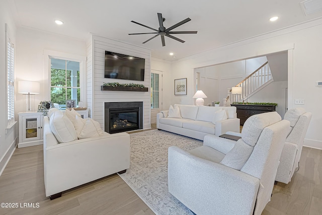 living area featuring a ceiling fan, visible vents, wood finished floors, baseboards, and ornamental molding