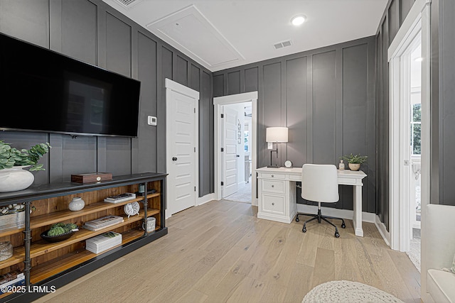 office with light wood finished floors, a decorative wall, attic access, baseboards, and visible vents