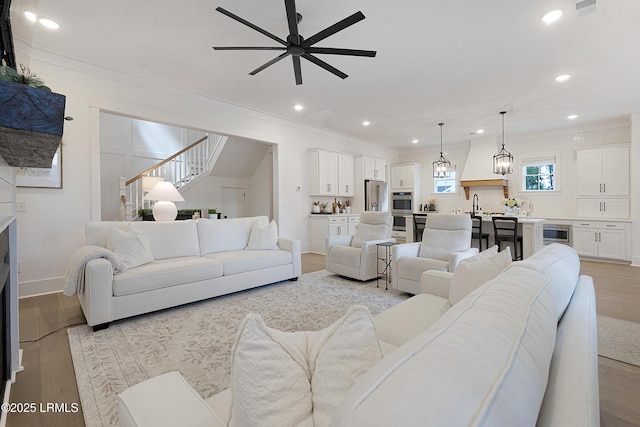 living area featuring crown molding, ceiling fan, stairway, recessed lighting, and light wood-style flooring