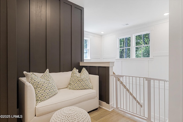 living area featuring light wood-style floors, an upstairs landing, visible vents, and a decorative wall