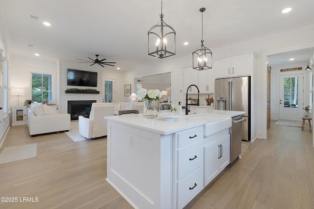 kitchen featuring white cabinets, appliances with stainless steel finishes, a sink, a fireplace, and ceiling fan with notable chandelier