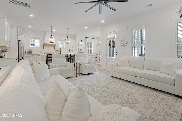 living area with crown molding, recessed lighting, ceiling fan with notable chandelier, and visible vents