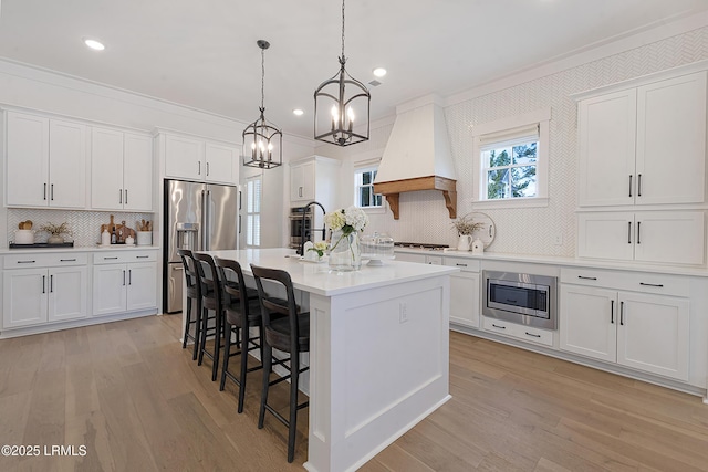kitchen featuring crown molding, appliances with stainless steel finishes, premium range hood, decorative backsplash, and a center island with sink