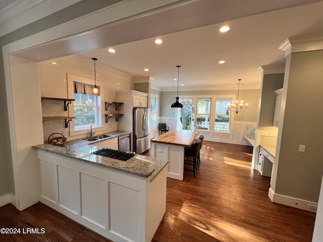 kitchen with appliances with stainless steel finishes, kitchen peninsula, hanging light fixtures, and white cabinets