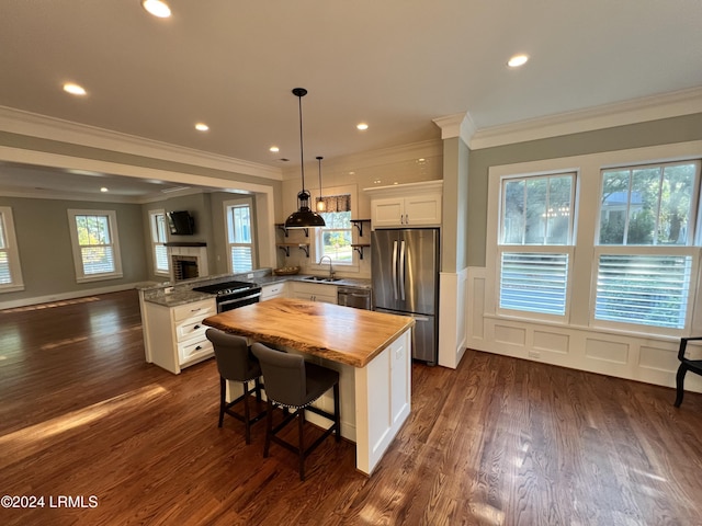 kitchen with appliances with stainless steel finishes, butcher block countertops, sink, white cabinets, and a kitchen bar