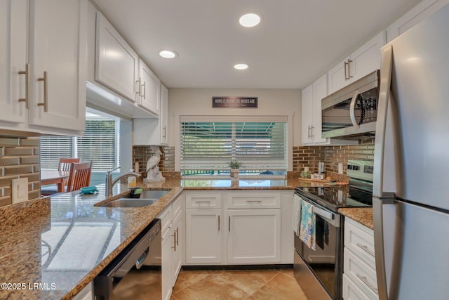 kitchen with sink, appliances with stainless steel finishes, white cabinetry, light stone counters, and decorative backsplash