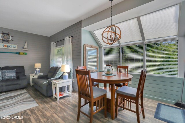 dining space with a healthy amount of sunlight, wooden walls, a chandelier, and hardwood / wood-style floors