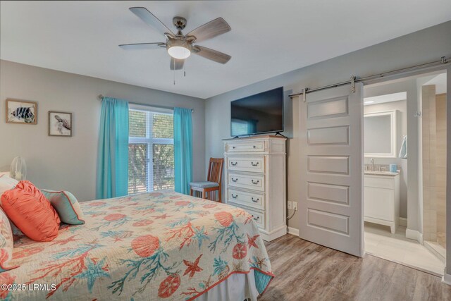 bedroom featuring ceiling fan, a barn door, light hardwood / wood-style floors, and ensuite bath