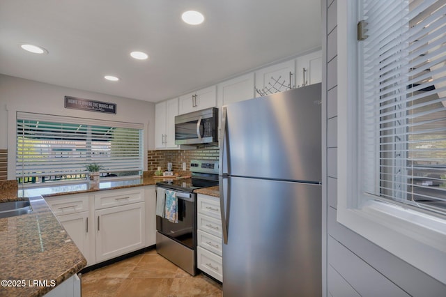 kitchen featuring stainless steel appliances, white cabinetry, dark stone countertops, and backsplash