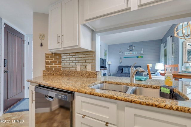 kitchen featuring tasteful backsplash, black dishwasher, sink, white cabinets, and light stone countertops