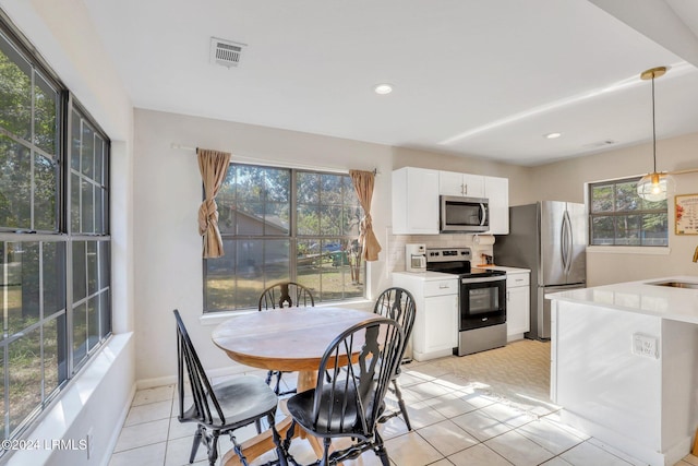 kitchen featuring sink, backsplash, stainless steel appliances, white cabinets, and decorative light fixtures