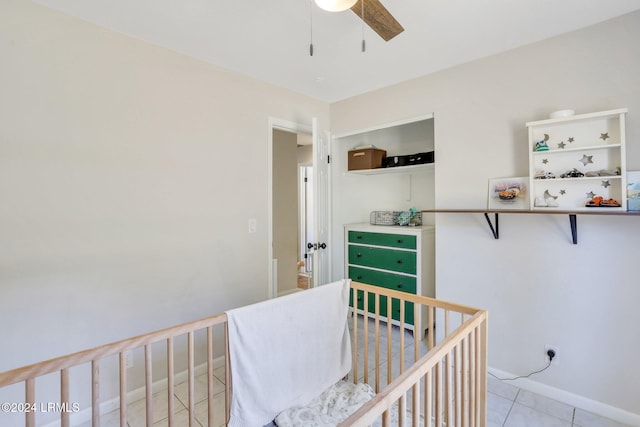 bedroom with a nursery area, light tile patterned floors, and ceiling fan