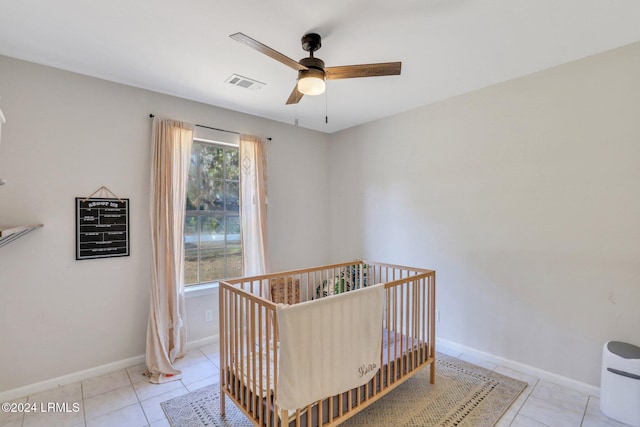 tiled bedroom featuring a nursery area and ceiling fan