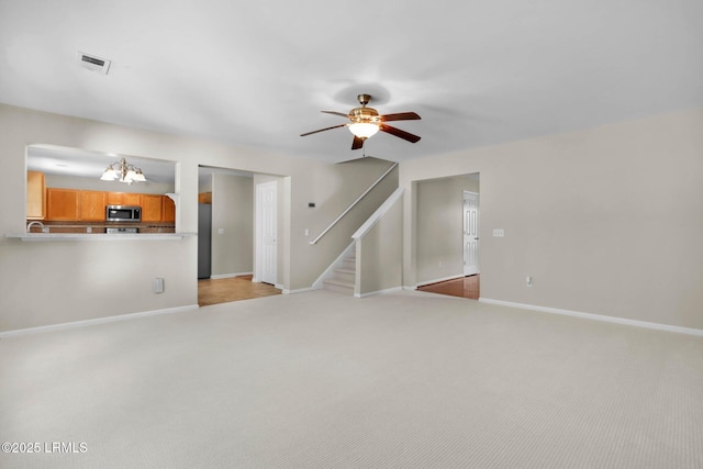 unfurnished living room with light colored carpet and ceiling fan with notable chandelier