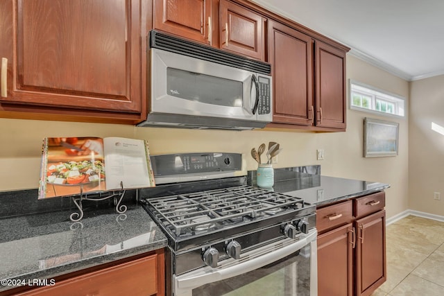 kitchen with dark stone countertops, ornamental molding, light tile patterned flooring, and appliances with stainless steel finishes