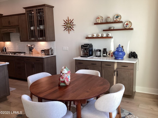 interior space with tasteful backsplash, dark brown cabinetry, stainless steel gas stovetop, and light hardwood / wood-style floors