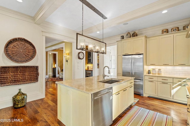 kitchen featuring an island with sink, appliances with stainless steel finishes, beamed ceiling, hanging light fixtures, and a sink