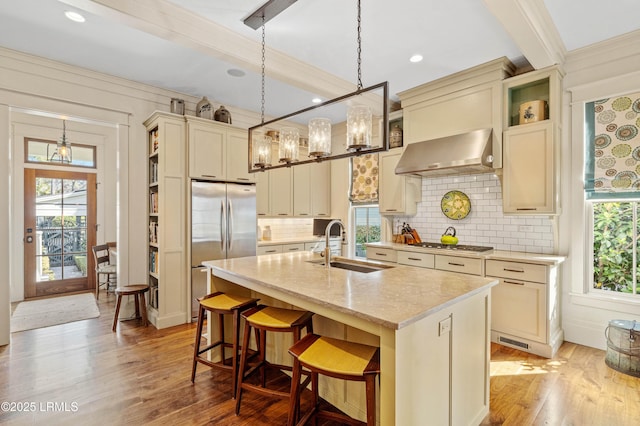 kitchen featuring a breakfast bar area, stainless steel appliances, hanging light fixtures, an island with sink, and wall chimney exhaust hood