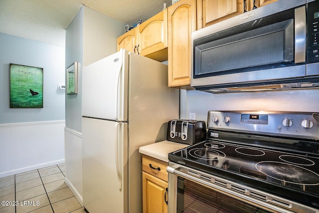 kitchen with light tile patterned flooring, stainless steel appliances, a textured ceiling, and wood walls