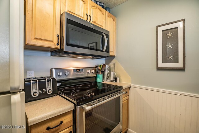 kitchen featuring appliances with stainless steel finishes, light brown cabinetry, a textured ceiling, and wood walls