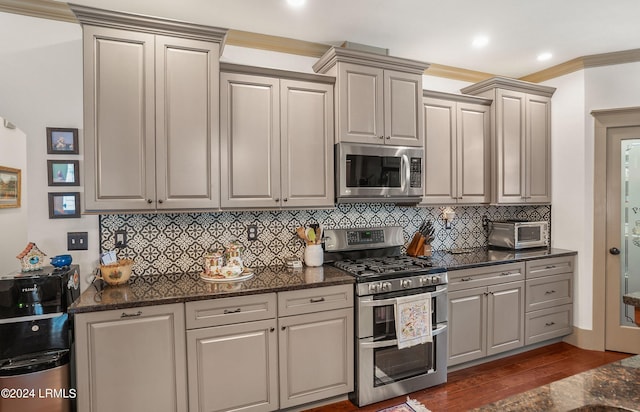 kitchen with appliances with stainless steel finishes, decorative backsplash, dark stone counters, crown molding, and dark wood-type flooring