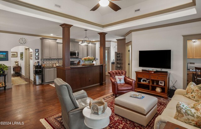 living room featuring dark wood-type flooring, ceiling fan, crown molding, and decorative columns