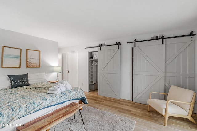 bedroom with a walk in closet, a barn door, a closet, and light hardwood / wood-style flooring