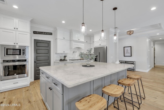 kitchen with white cabinetry, decorative light fixtures, appliances with stainless steel finishes, a kitchen breakfast bar, and a kitchen island