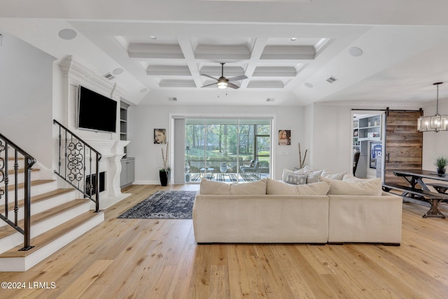 living room with coffered ceiling, beam ceiling, light hardwood / wood-style flooring, a barn door, and ceiling fan with notable chandelier