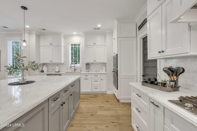 kitchen with sink, white cabinetry, hanging light fixtures, light stone countertops, and light hardwood / wood-style floors