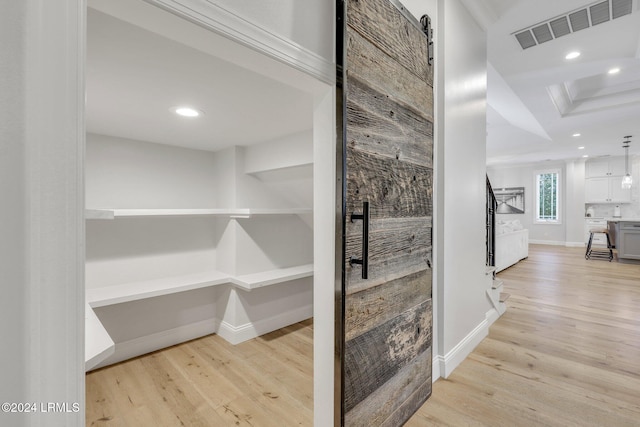 wine cellar featuring crown molding, a barn door, a raised ceiling, and light hardwood / wood-style floors