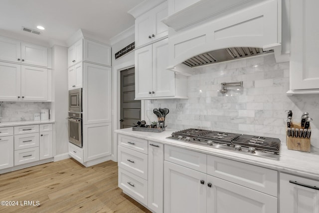 kitchen featuring white cabinetry, appliances with stainless steel finishes, custom range hood, light hardwood / wood-style floors, and backsplash