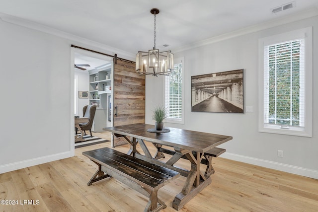 dining area featuring a wealth of natural light, light hardwood / wood-style flooring, ornamental molding, and a barn door