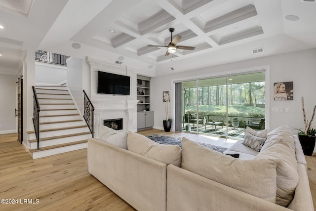 living room with beamed ceiling, a large fireplace, coffered ceiling, ceiling fan, and light wood-type flooring