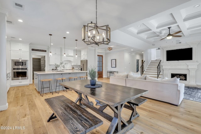 dining space featuring coffered ceiling, ceiling fan with notable chandelier, beam ceiling, and light wood-type flooring