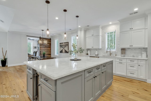 kitchen featuring sink, light stone counters, a center island, hanging light fixtures, and light hardwood / wood-style floors