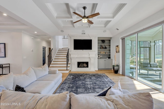 living room featuring coffered ceiling, light wood-type flooring, ornamental molding, beamed ceiling, and ceiling fan