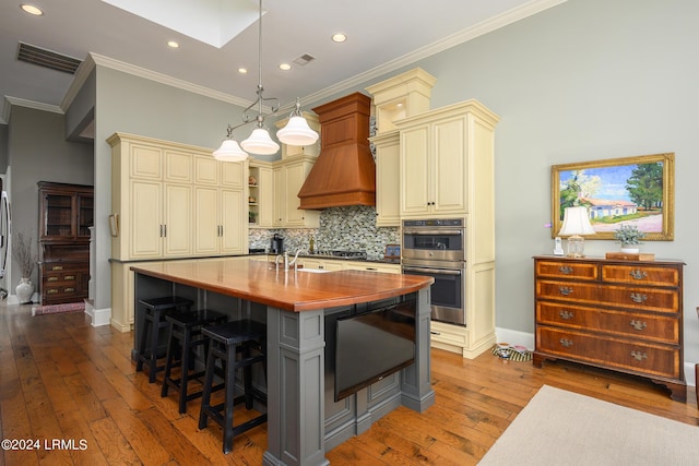 kitchen with cream cabinets, a breakfast bar, hanging light fixtures, appliances with stainless steel finishes, and a kitchen island with sink