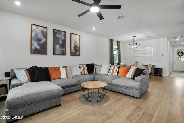 living room featuring ceiling fan with notable chandelier and light hardwood / wood-style flooring