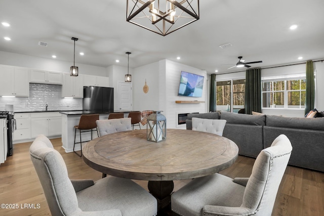 dining area with ceiling fan, a fireplace, sink, and light hardwood / wood-style flooring