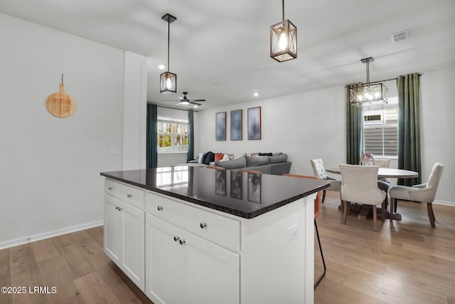 kitchen with a kitchen island, a breakfast bar area, white cabinets, hanging light fixtures, and light wood-type flooring