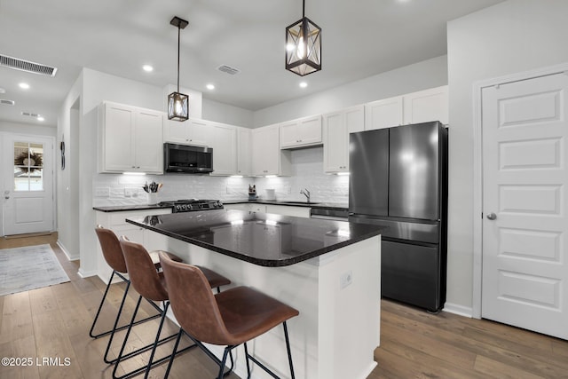 kitchen featuring a center island, stainless steel refrigerator, a kitchen breakfast bar, pendant lighting, and white cabinets