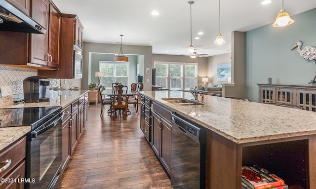 kitchen featuring pendant lighting, sink, a center island with sink, and black appliances