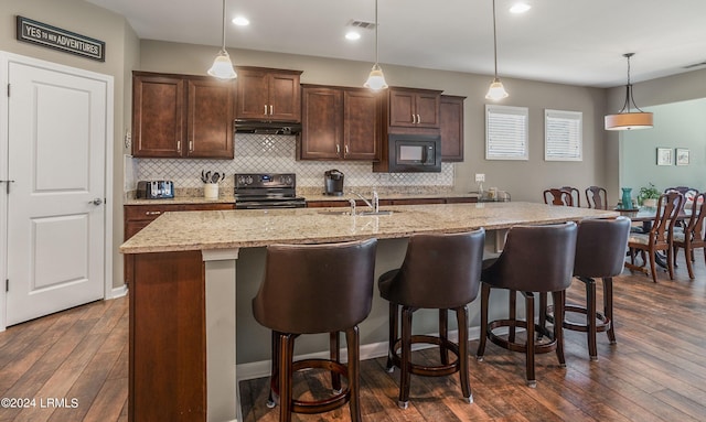 kitchen with pendant lighting, black microwave, an island with sink, sink, and electric stove