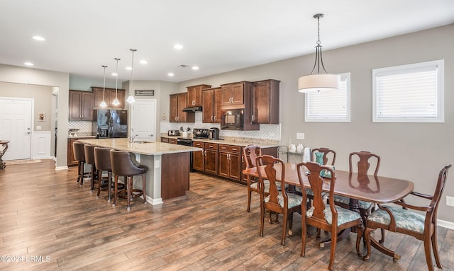 kitchen with light stone counters, decorative light fixtures, black appliances, and a kitchen bar